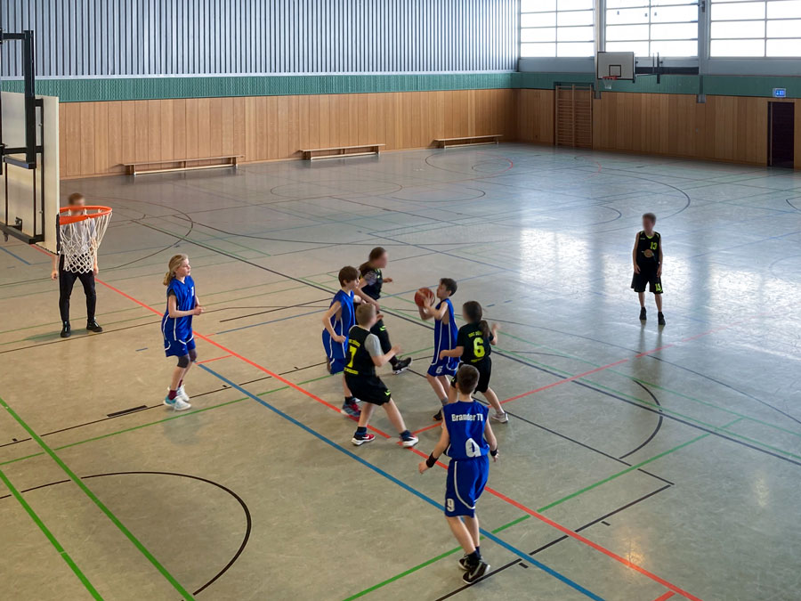Eine Gruppe von Kindern spielt Basketball in einer Turnhalle.