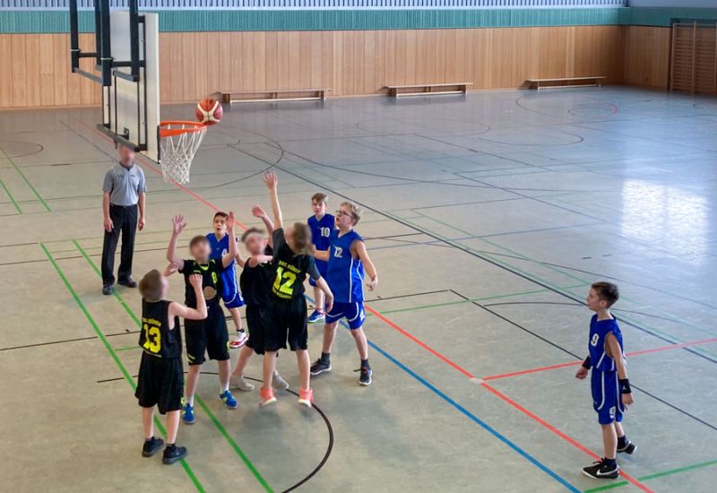 Eine Gruppe von Kindern spielt Basketball in einer Turnhalle.