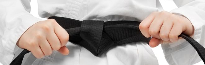 Judo-Anzug mit schwarzen Gürtel der mit Händen an den Schlaufen festgezogen wird