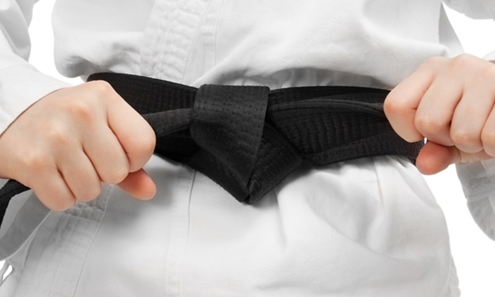 Judo-Anzug mit schwarzen Gürtel der mit Händen an den Schlaufen festgezogen wird